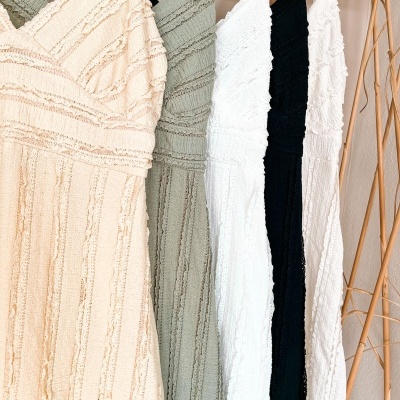 Vestidos texturados em bege, verde, branco e preto pendurados em cabides de madeira