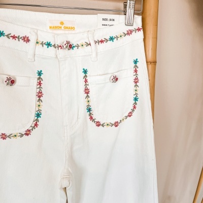 Calças brancas com bordados florais coloridos e botões forrados