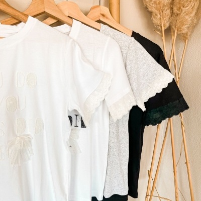 Quatro t-shirts com renda nas mangas penduradas em cabides de madeira