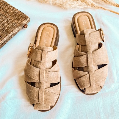 Sandálias bege de camurça com fivela dourada sobre tecido branco e bolsa de palha