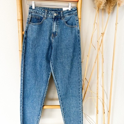 Calças de ganga azuis penduradas em escada de bambu com ramos secos ao lado