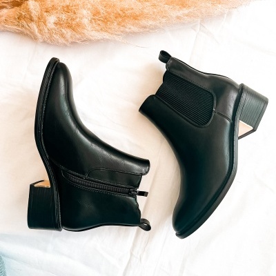 Botas pretas de pele com salto médio e elástico lateral sobre tecido branco