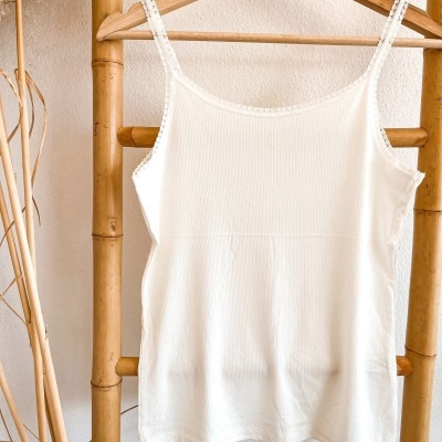 Top branco de alças finas pendurado num cabide de madeira no bambu