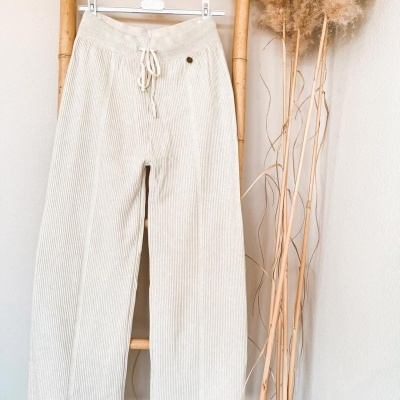 Calças creme claro de tecido canalé penduradas num cabide numa escada de bambu.