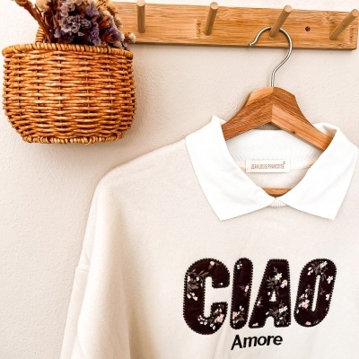 Casaco bege claro com gola branca e texto floral pendurado num cabide de madeira