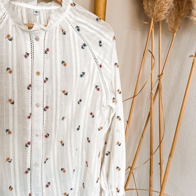 Blusa branca com bordados florais coloridos pendurada em cabide de madeira