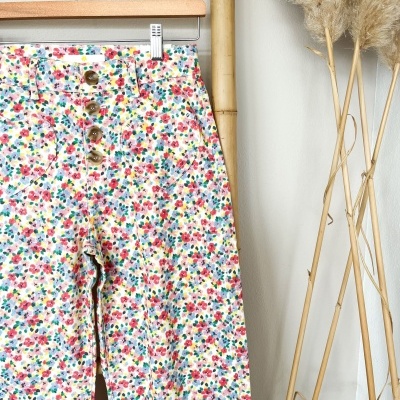 Calças florais coloridas com botões marrons penduradas num cabide de madeira