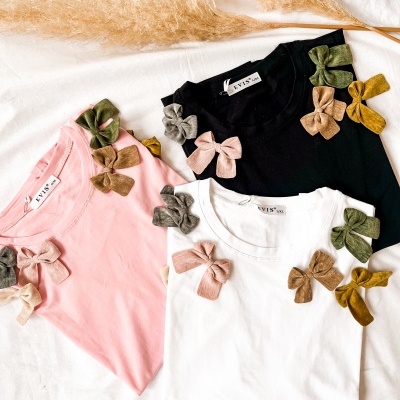 Três t-shirts coloridas com laços de tecido decorativos e ramos decorativos