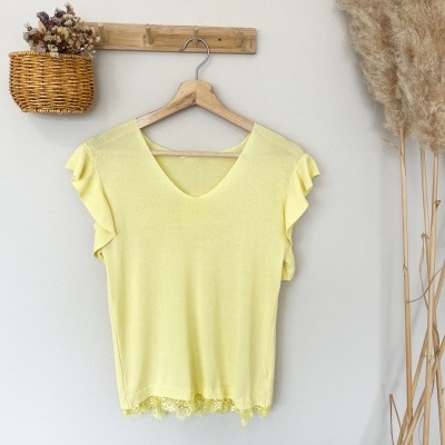 T-shirt amarela com detalhes em renda pendurada com cabide de madeira numa parede branca