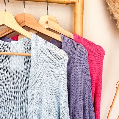 Camisolas de malha azul claro, roxa e rosa penduradas em cabides de madeira