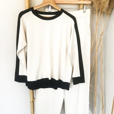 Conjunto roupa branco com detalhes pretos pendurado em suporte de bambu