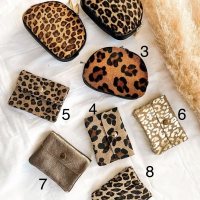 Oito carteiras pequenas numeradas com padrão animal print em tons de castanho, bege e preto sobre tecido branco.