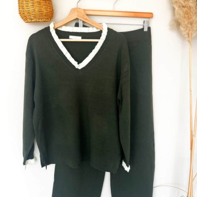 Conjunto de roupa de malha castanha escura com detalhes brancos pendurado em cabideiro.