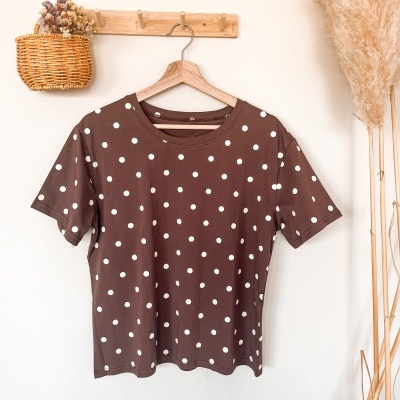 T-shirt castanha com bolinhas brancas pendurada na parede.