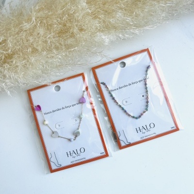 Duas pulseiras coloridas em cartões com texto motivacional e decoração em plumas secas