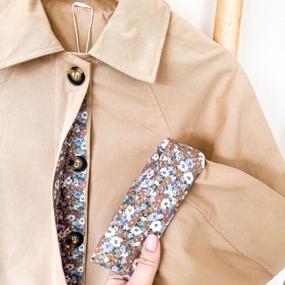 Casaco bege com forro floral e botões pretos num cabide de madeira