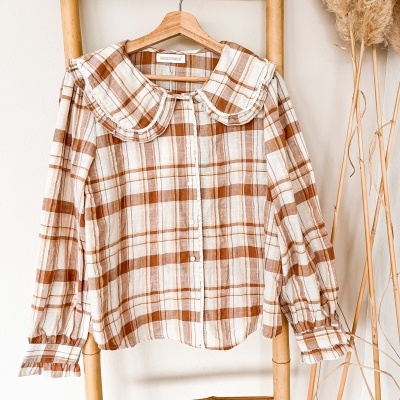 Blusa xadrez branca e castanha com gola grande pendurada numa escada de bambu