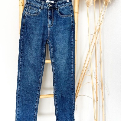 Calças de ganga azuis penduradas num cabide sobre uma escada de bambu com plantas secas ao lado