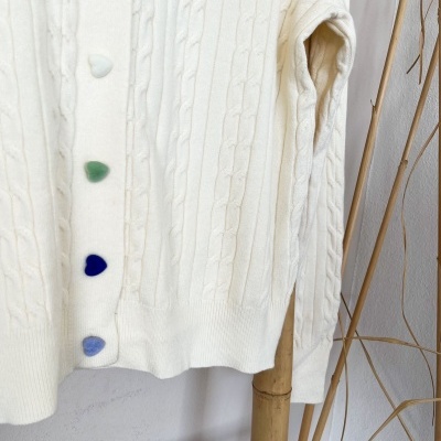 Camisola branca de malha com botões em forma de corações coloridos.