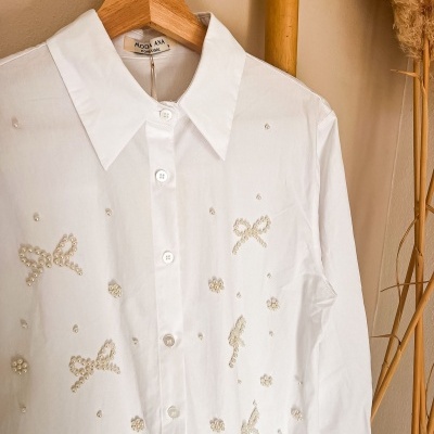Camisa branca com pérolas e botões pendurada num cabide de madeira