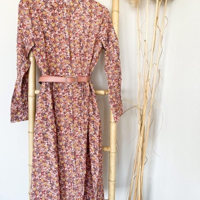 Vestido comprido floral com cinto laranja pendurado em suporte de bambu e decoração seca ao lado