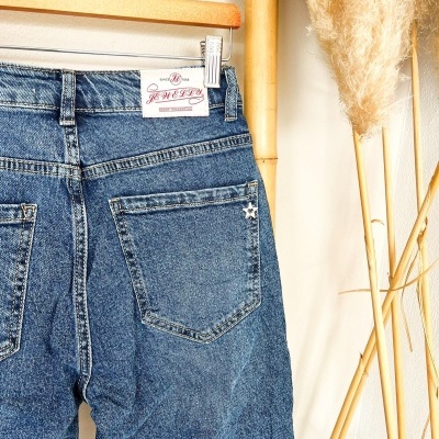 Calças de ganga azuis penduradas num cabide de madeira com etiqueta JEWELRY