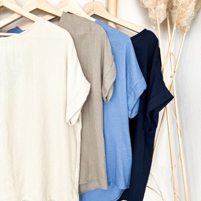 Quatro blusas de manga curta em tons neutros penduradas em cabides de madeira