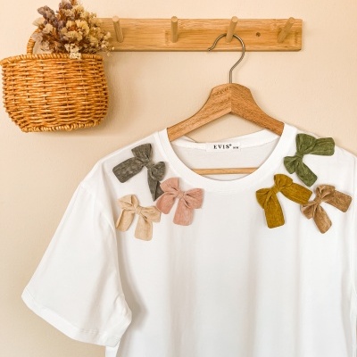 T-shirt branca com laços coloridos pendurada em cabide de madeira num cabideiro de parede em madeira com cesto de vime e flores secas