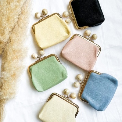 Seis carteiras pequenas de pele coloridas com fechos dourados e bolas decorativas, sobre tecido branco