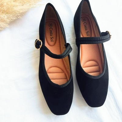 Par de sapatos pretos com tira e fivela dourada em fundo branco