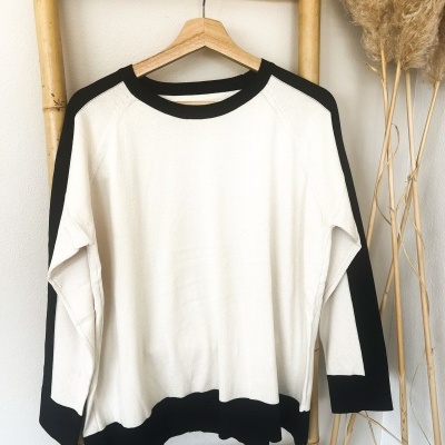 Camisola branca com detalhes pretos pendurada num cabide de madeira