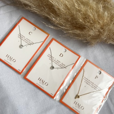 Colares com letras C, D e P em cartão branco com borda laranja sobre tecido cinzento claro.