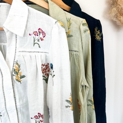 Camisas de linho com bordado floral penduradas em cabides de madeira