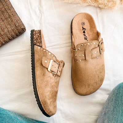 Chinelos bege com fivela dourada sobre toalha branca, mala de palha castanha e calças de ganga azuis.