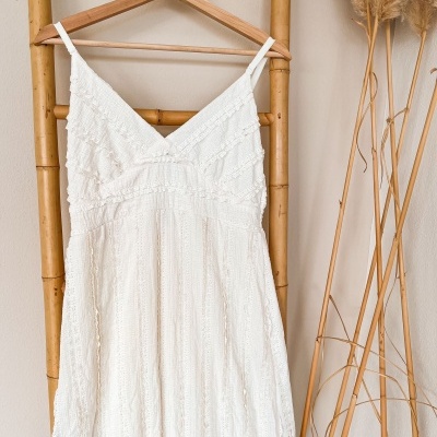 Vestido branco de alças finas pendurado num cabide de madeira num varão de bambu com decoração seca ao lado