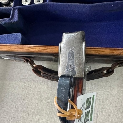 Caixa de madeira com interior azul e cápsulas metálicas, com trava metálica e alça de couro com cartão e elástico.