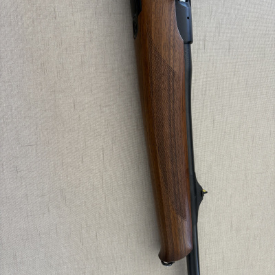 Rifle em madeira castanha e metal preto sobre fundo cinza