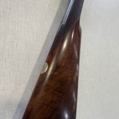 Coronha de espingarda em madeira castanha com punho texturizado escuro e medalha metálica embutida