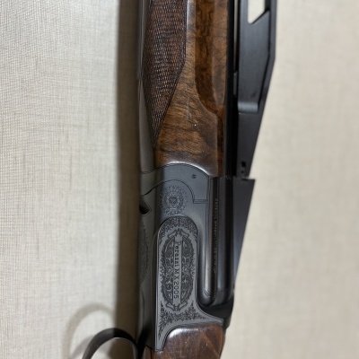 Espingarda Perazzi MX2005 com madeira castanha e metal gravado, gatilho dourado.