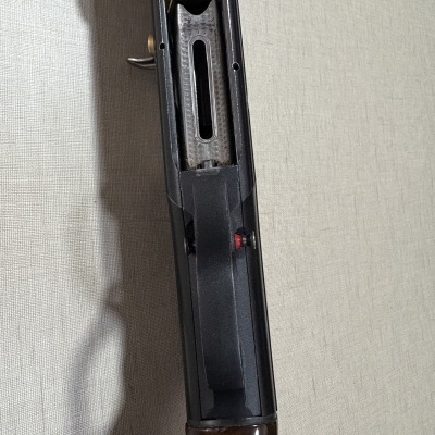 Arma de fogo com corpo preto e empunhadura em madeira, vista de perto