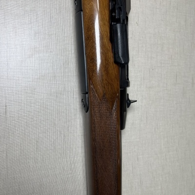 Espingarda com coronha de madeira e metal preto num fundo cinza claro