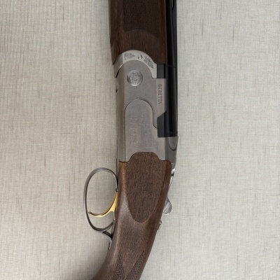 Espingarda Beretta com madeira castanha escura e metal gravado em fundo cinzento.