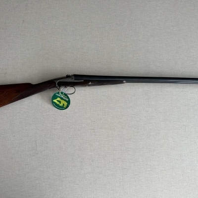 Espingarda com canos pretos, coronha de madeira castanha e etiqueta verde pendurada
