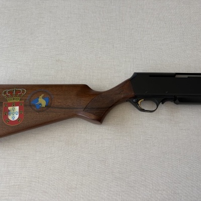 Espingarda com coronha em madeira castanha com duas estampas e parte metálica preta.