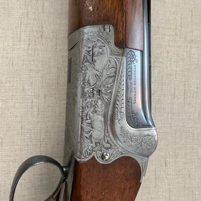 Detalhe da caixa metálica gravada e madeira de uma espingarda