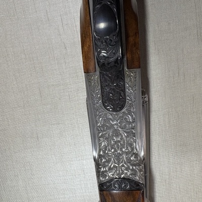 Espingarda de caça com detalhes gravados em metal e madeira castanha sobre fundo cinza claro