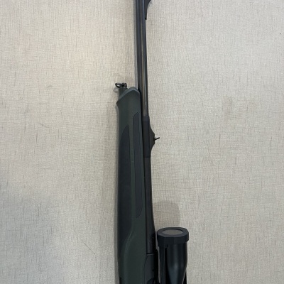 Rifle de ar comprimido verde-escuro com luneta preta encostado numa parede clara