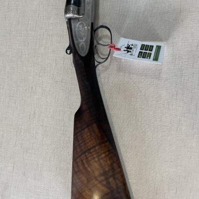 Espingarda de caça com coronha em madeira escura e canos pretos com etiqueta pendurada