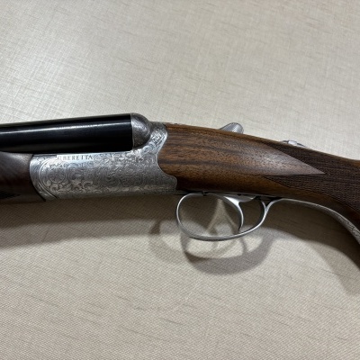 Espingarda dupla Beretta com caixa prateada gravada, canos pretos e madeira escura entalhada