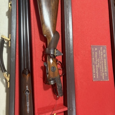 Espingarda desmontada numa caixa vermelha com etiqueta e placa bordada